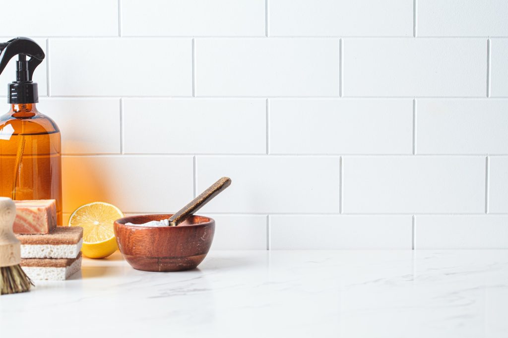 Natural brushes, sponges and organic cleaning products on white kitchen table.